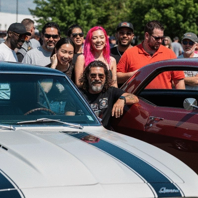 Enthusiasts gathered around a classic car at an outdoor car show, bright sunny day, no text, no words, no typography, 8K